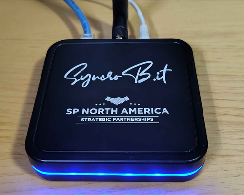SyncroBit reassembled and powered on with antenna, network, and power connected and the blue LED ring lit